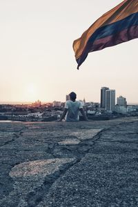 Rear view of man sitting and looking at view against clear sky