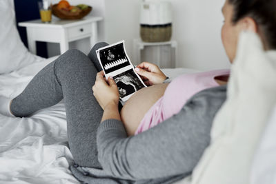 Midsection of woman using mobile phone on bed at home
