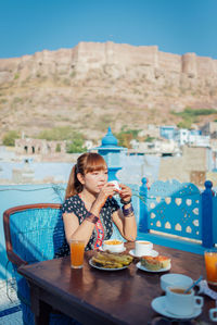 Woman having food while sitting at restaurant against fort