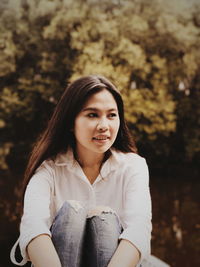 Thoughtful woman looking away while sitting against tree