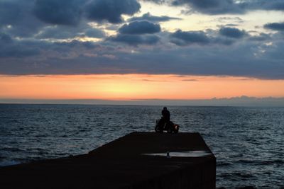 Silhouette man sitting on beach against sky during sunset