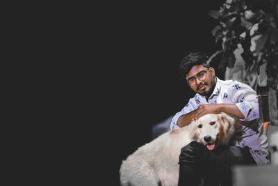 Portrait of young man with dog against black background