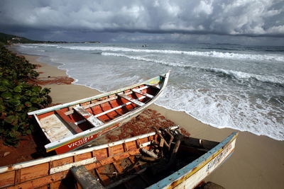 Boats moored at sea shore against cloudy sky