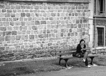 Man sitting on bench against brick wall