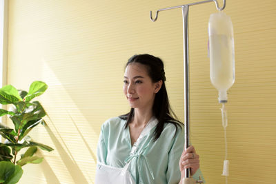 Smiling woman with iv drip standing against wall