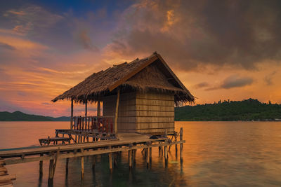 Stilt house by lake against sky during sunset