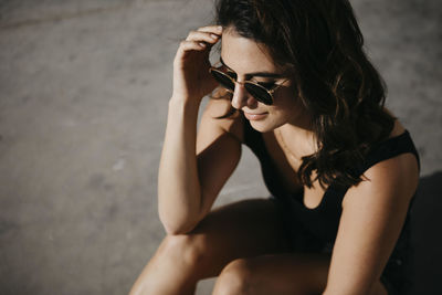 Thoughtful woman sitting on concrete footpath during sunny day