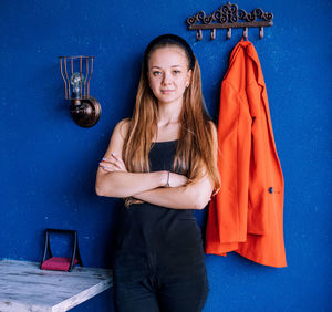 A young woman on the background of a blue wall. a red jacket hangs nearby. a glance to the side.