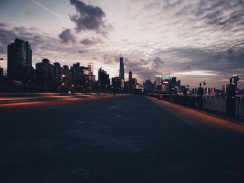 Illuminated city street and buildings against sky at sunset