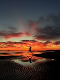 Silhouette of woman jumping on beach at sunset
