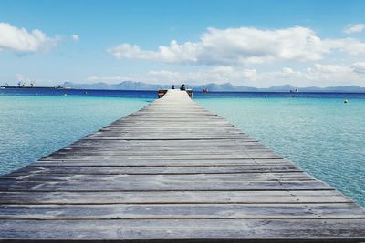 Empty jetty leading to sea against cloudy sky