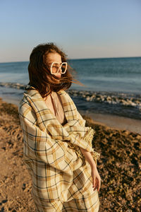 Young woman standing at beach against sky