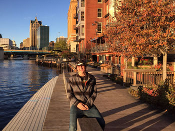 Young man sitting by lake on retaining wall in city