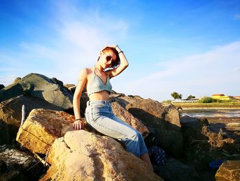 Young woman sitting on rock against sky