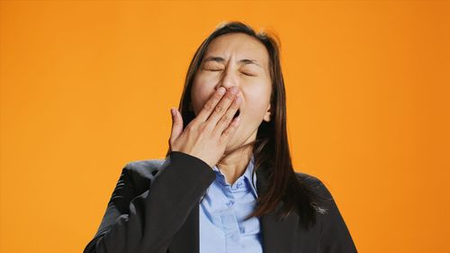 Young woman standing against yellow background