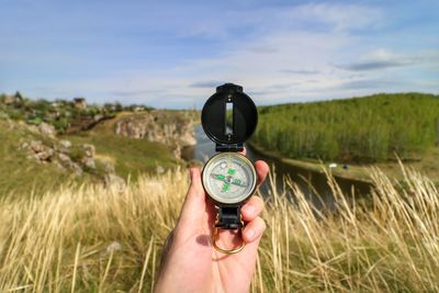 Cropped hand holding compass against field