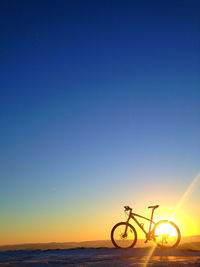 Bicycle parked at beach against clear blue sky during sunset