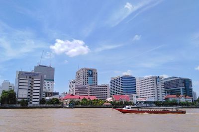 Buildings by river against blue sky