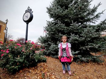 Girl standing by clock against tree at park