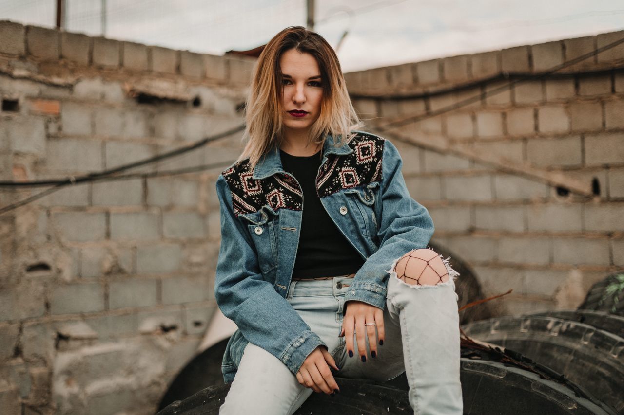 BEAUTIFUL YOUNG WOMAN SITTING WITH UMBRELLA IN FRONT OF BUILT STRUCTURE