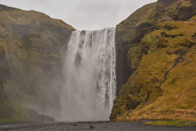 Scenic view of waterfall by sea against mountain