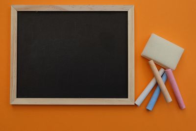 Directly above shot of chalk and writing slate on orange background