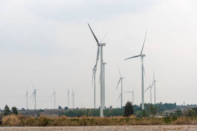 Windmills on field against cloudy sky