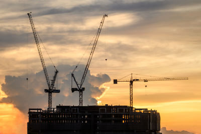 Low angle view of silhouette cranes against sky during sunset