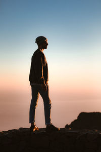 Silhouette man standing on rock against sky during sunset