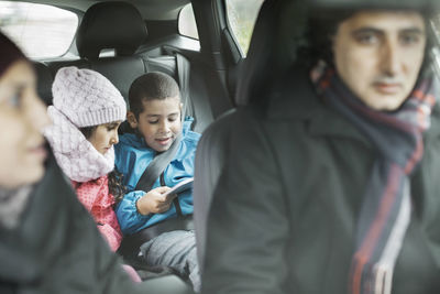 Siblings using digital tablet while on road trip with parents