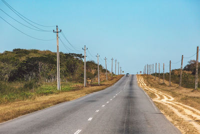 Road by electricity pylons against clear sky