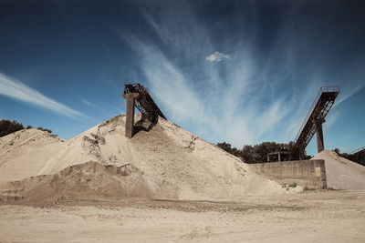 Low angle view of conveyor belt on sand pile at mine against sky