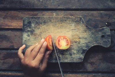 Cropped hand of person holding tomato by knife on table