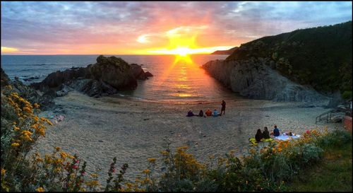 People on beach against sky during sunset