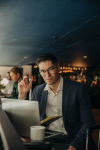 Portrait of businessman wearing eyeglasses sitting with laptop in hotel