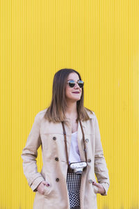 Young woman wearing sunglasses standing against yellow wall