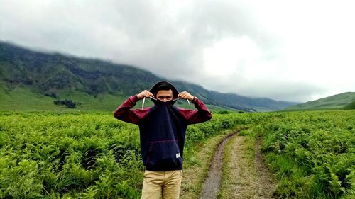 Portrait of young man standing amidst plants on field during foggy weather