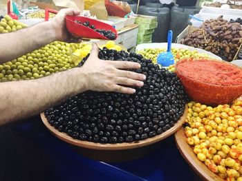 Cropped hands of vendor arranging olives for sale at market stall