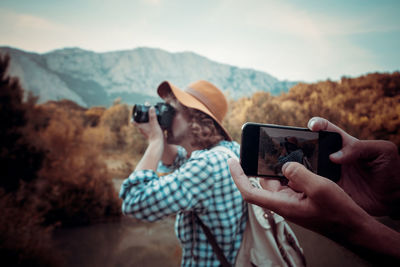 Man photographing with mobile phone against mountains