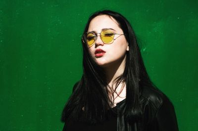 Close-up portrait of young woman standing against green background