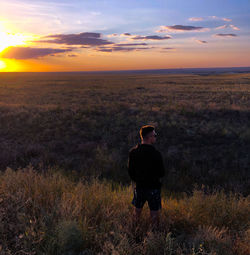 Rear view of man standing on field against sky during sunset