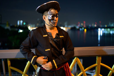 Young man wearing pirate costume standing on bridge against sky at night