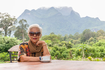 Asin grey white hair senior woman drinking coffee in cafe outdoor with mountain view