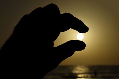 Silhouette hand against sky during sunset