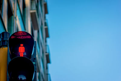 Low angle view of red light on road signal against blue sky