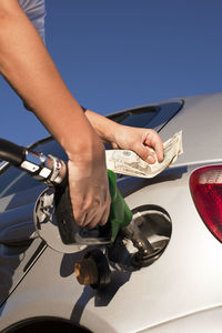 Cropped image of man refueling car while holding currency in hand