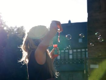 Side view of woman making bubbles against building and sky