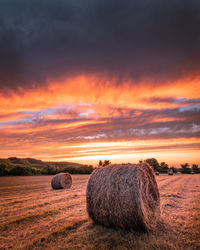 Hay bales on field against sky during sunset