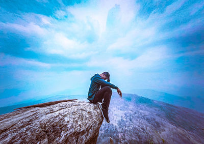 Young man on rock against sky