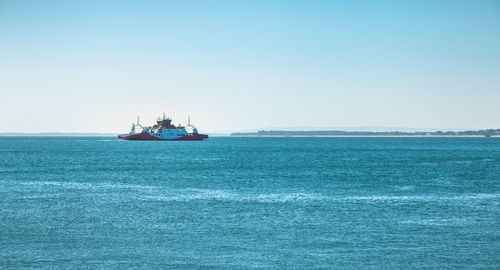 Boat sailing in sea against clear blue sky